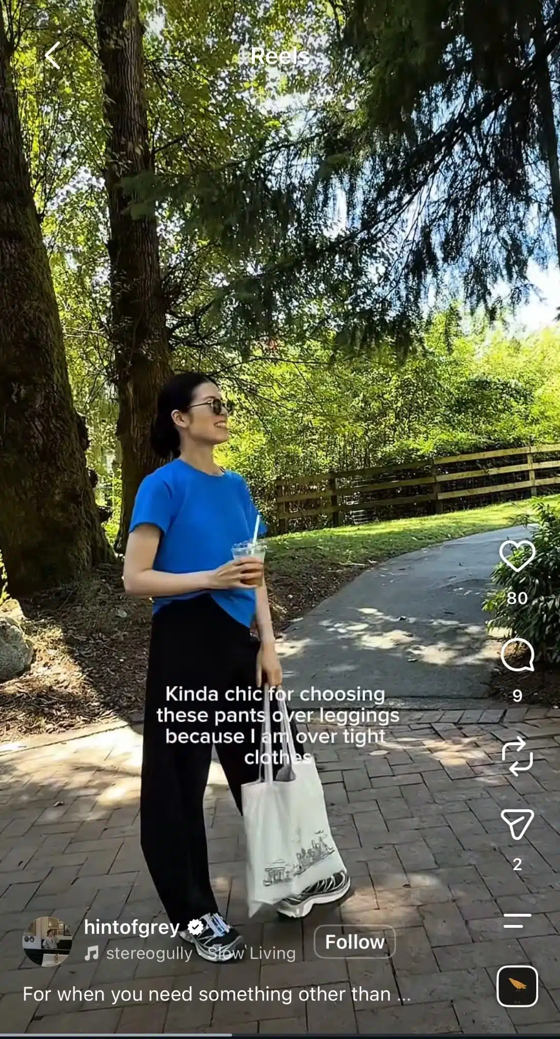Woman holding an iced drink and tote bag outdoors with text reading “Kinda chic for choosing these pants over leggings because I am over tight clothes,” using the “Slow Living” audio trend.