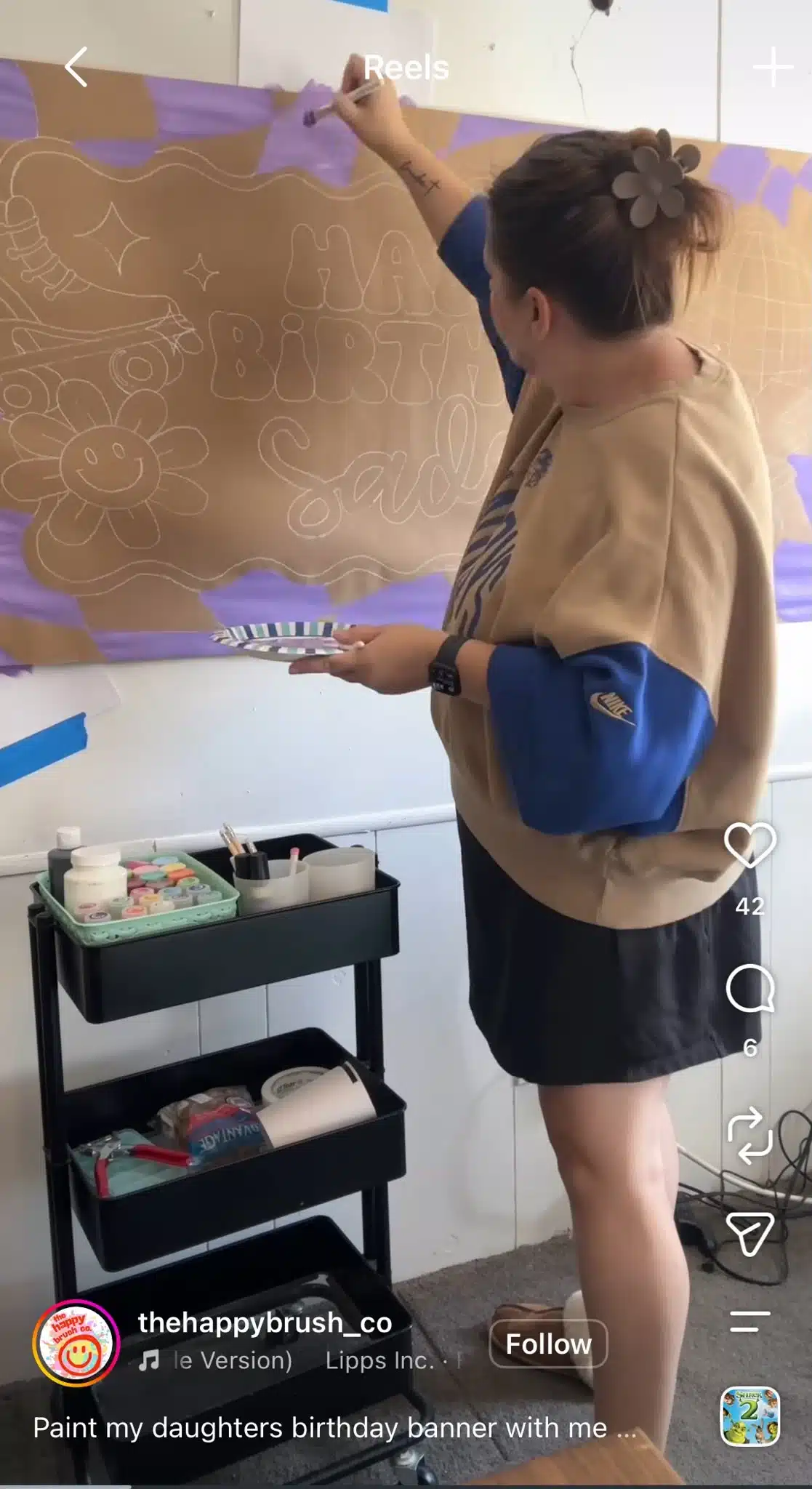 Instagram Reel from The Happy Brush Co showing a woman painting a handmade birthday banner with colorful craft supplies beside her.