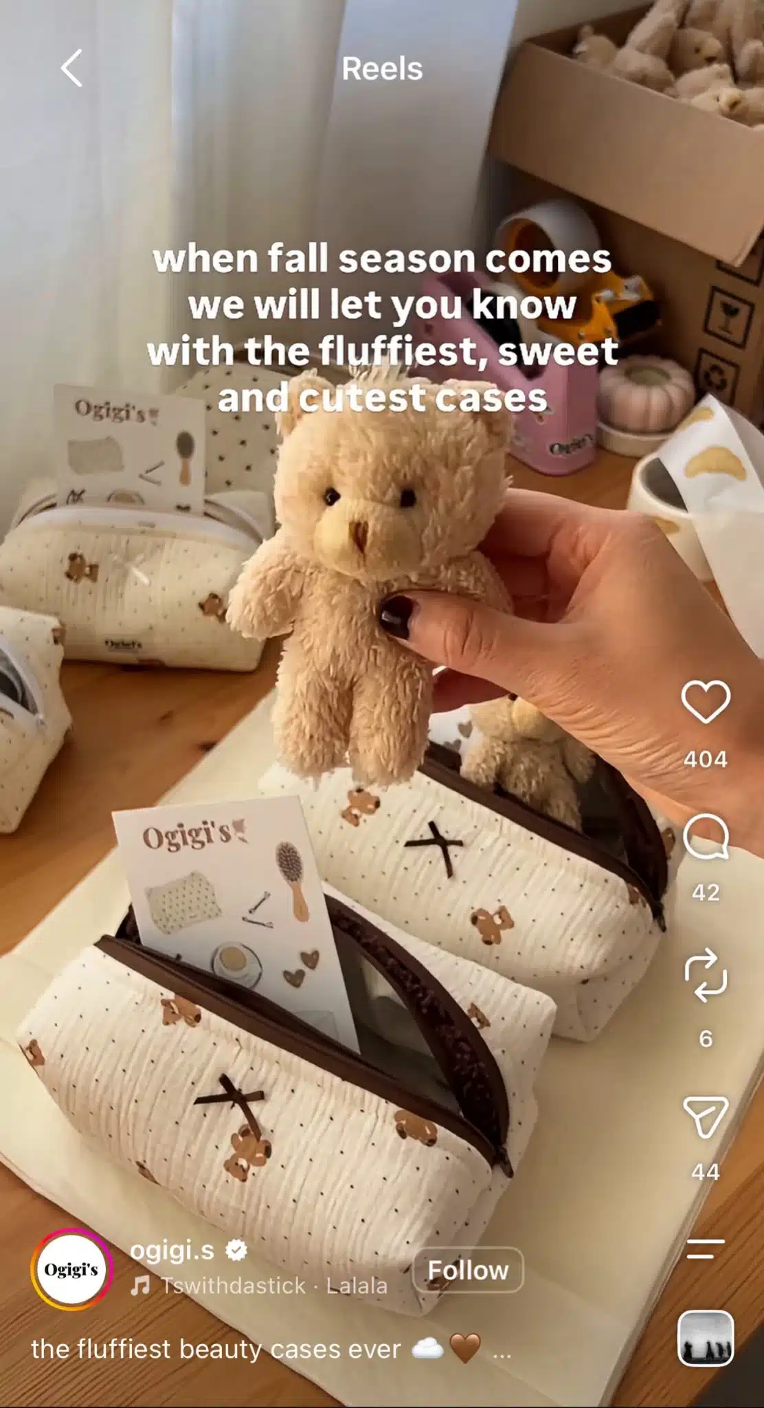 Instagram Reel from Ogigi's showing a hand holding a small teddy bear above a collection of cream-colored beauty cases, with text promoting the brand's fall collection.