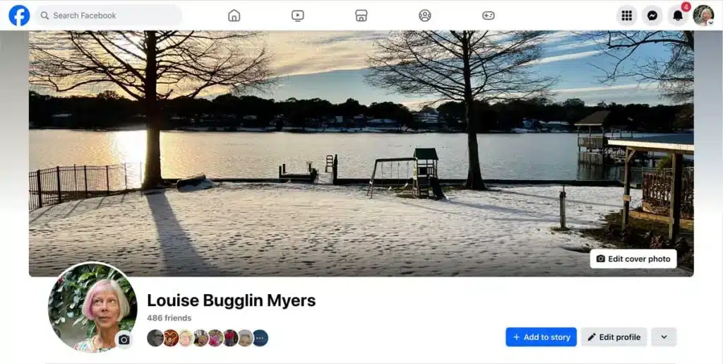 Facebook profile page featuring a winter lakeside cover photo. The cover image shows a snow-covered yard leading to a calm lake, with bare trees casting long shadows in the foreground. A small dock, playground structure, and waterfront boathouses are visible along the shoreline under a partly cloudy sky. Below the cover photo is a circular profile picture and the profile header with friend count and profile management buttons.
